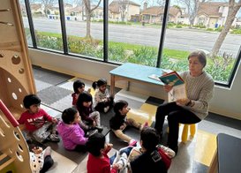Teacher reading to children in a bright Montessori classroom in Bay Area with a large window view.