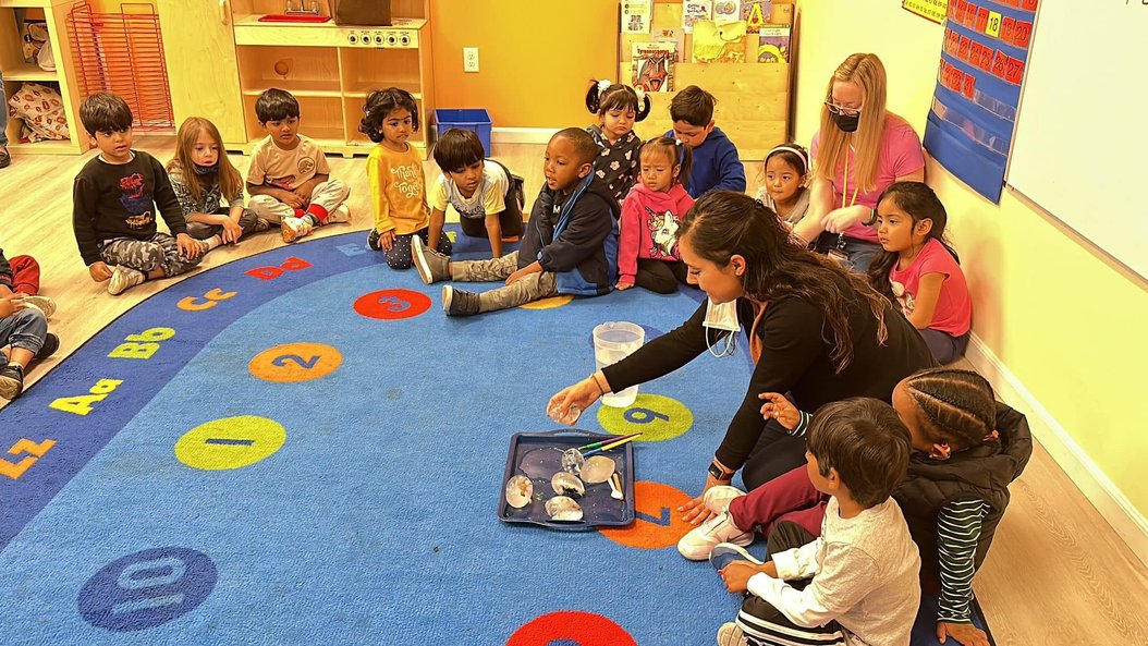Montessori teacher engaging children in activities to build confidence and early academic skills on a colorful rug.