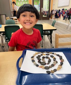 Child smiling at a Montessori school with a rock spiral on a tray.