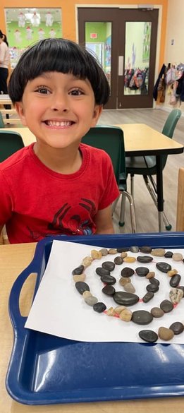 Child smiling at a Montessori school with a rock spiral on a tray.