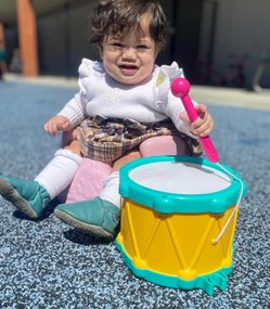 Infant playing with a toy drum at Level Up Montessori, illustrating nurturing and child-focused growth.