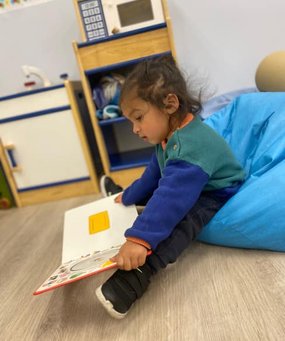 Infant reading a book at Level Up Montessori, promoting early growth and discovery.