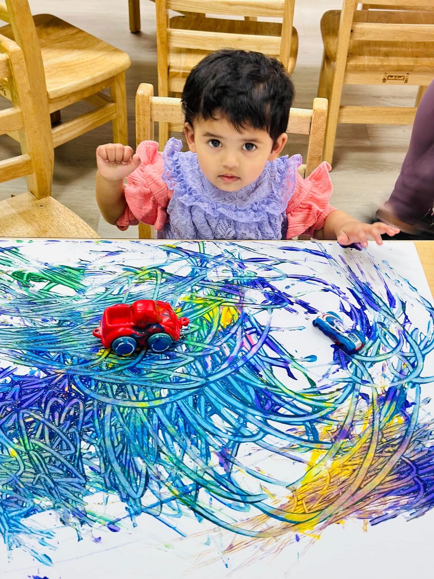 Kindergartner at Level Up Montessori engaging in art activity with colorful drawings and toy cars.