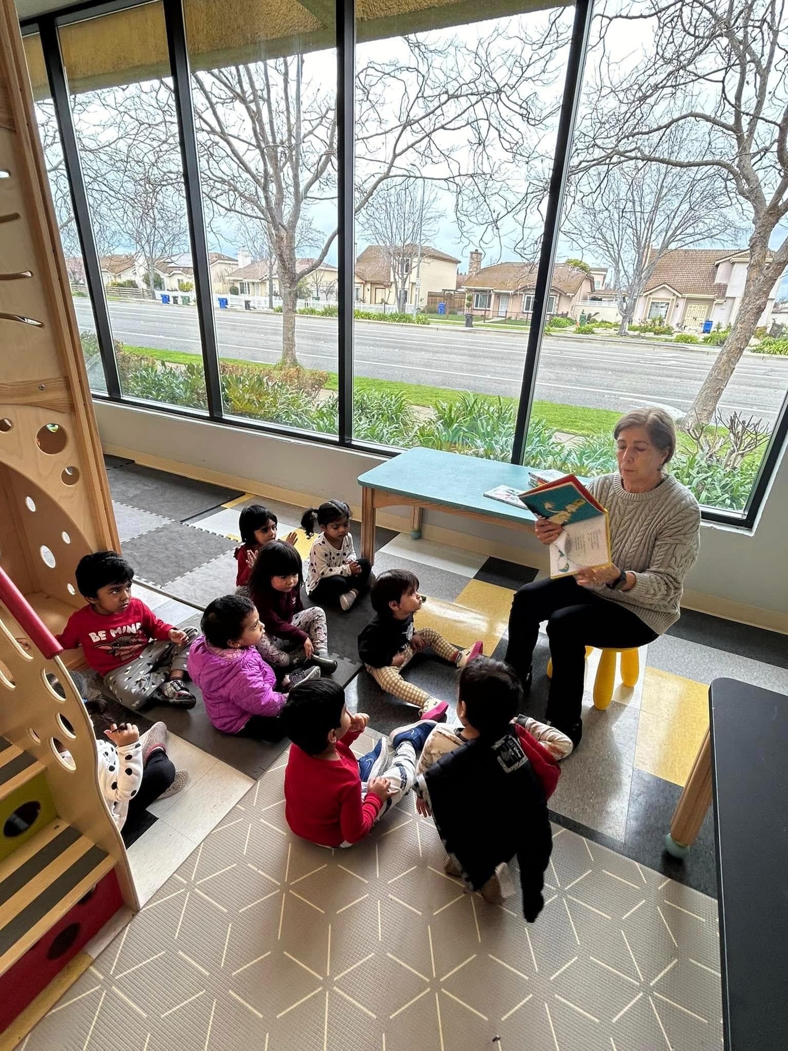 Teacher reading to children in a bright Montessori classroom in Bay Area with a large window view.